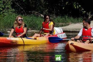 Grupo de personas en kayaks disfrutando de una actividad recreativa en un río, rodeados de naturaleza. Se observan tres individuos, todos usando chalecos salvavidas. Ideal para promover turismo de aventura y actividades al aire libre.