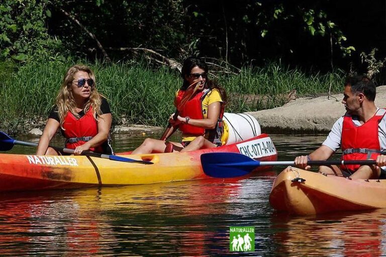 Grupo de personas en kayaks disfrutando de una actividad recreativa en un río, rodeados de naturaleza. Se observan tres individuos, todos usando chalecos salvavidas. Ideal para promover turismo de aventura y actividades al aire libre.