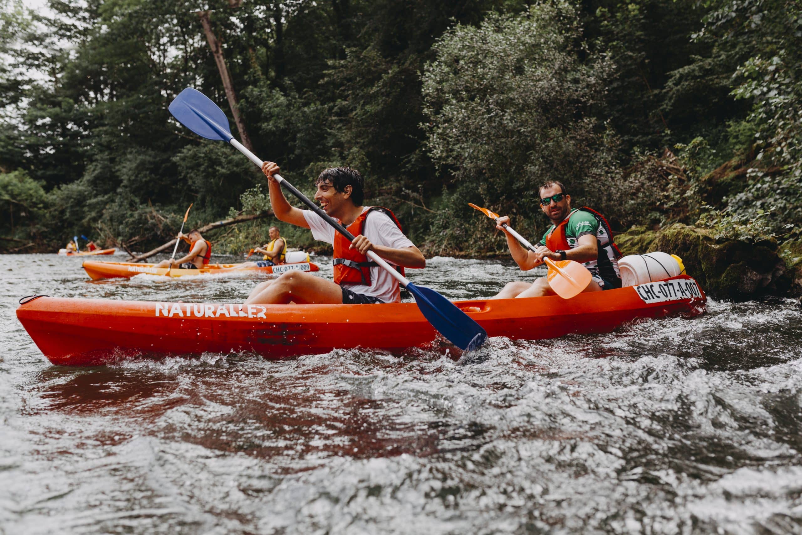 Personas haciendo piragüismo en río rodeado de bosque.