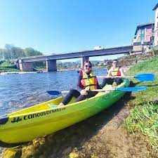 Personas en kayak sobre río con puente cercano.