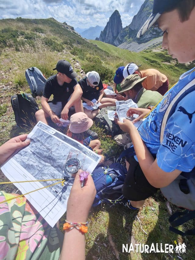 Grupo de personas jóvenes explorando un mapa y utilizando una brújula en un entorno montañoso. La actividad promueve el aprendizaje de habilidades de orientación y conexión con la naturaleza.