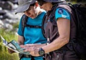 Dos personas revisan un mapa durante una actividad de senderismo en la naturaleza, mostrando la importancia de la navegación al aire libre.