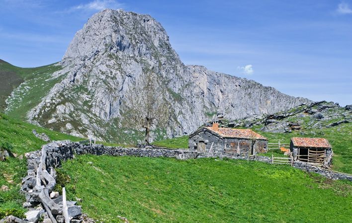 Cabaña rural en paisaje montañoso verde y rocoso.